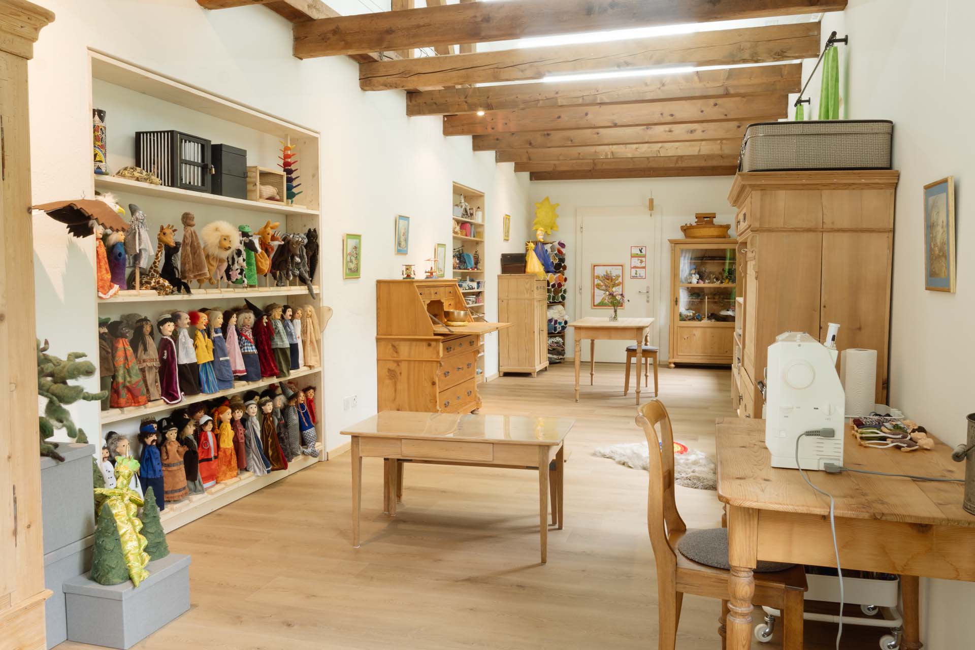 Heller, langer Praxisraum mit Holztisch in der Mitte und Holzmöbel auf der Seite. Blick auf die Figurenwand.