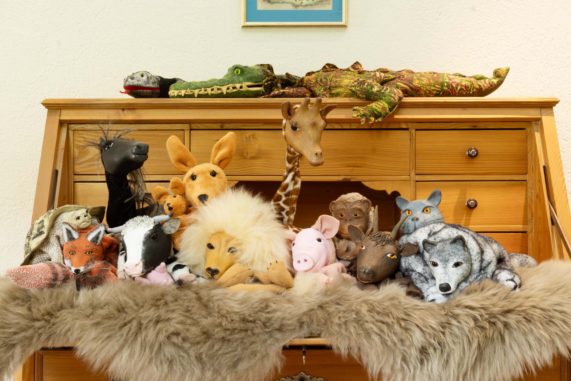 Regal voll mit Stofftieren und Figuren auf einem Fell. Zu den Tieren gehören ein Löwe, Giraffe, Katze, Krokodil, Schwein, Kuh, Affe, Pferd, Ziege, Schildkröte.