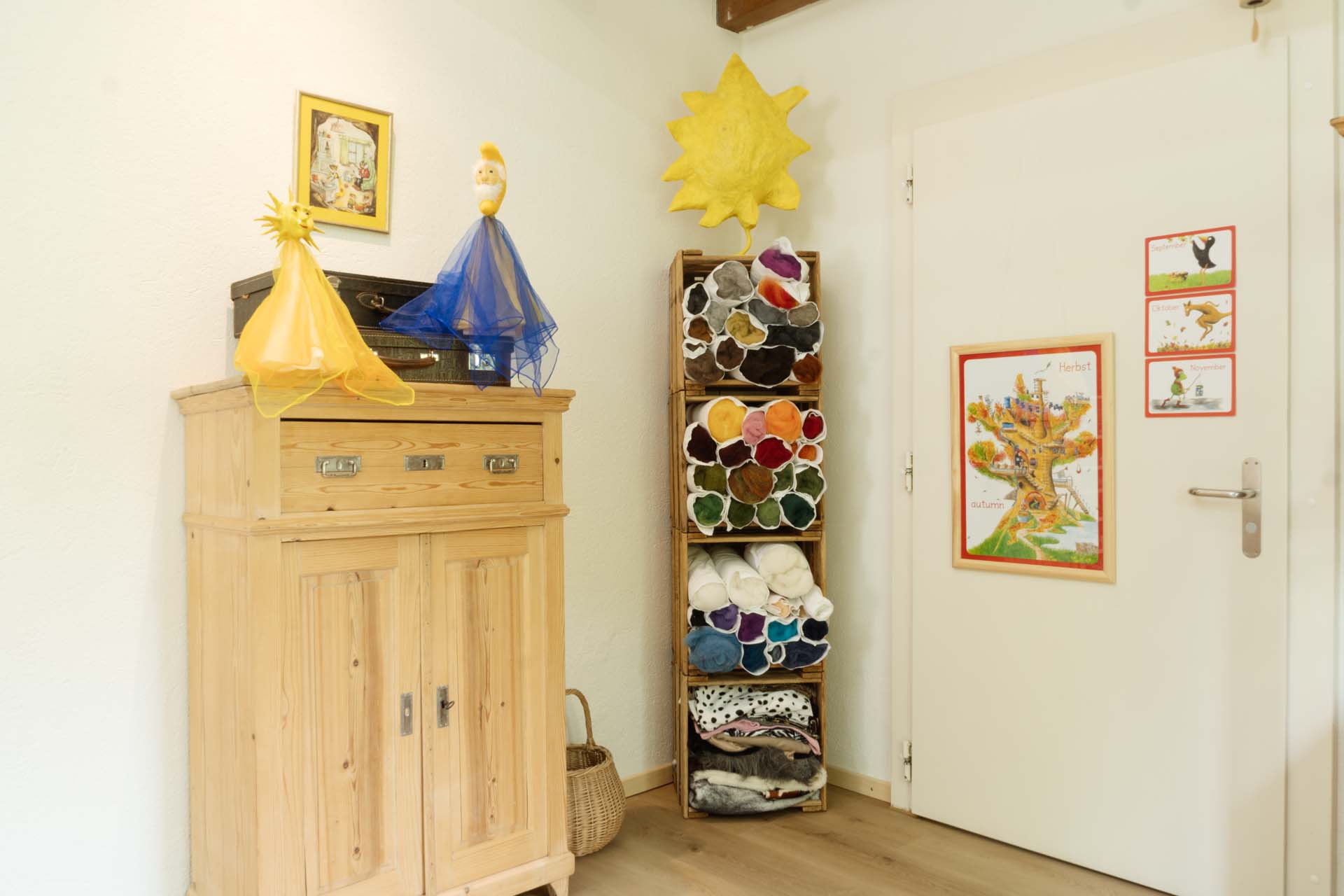 Blick auf die Ecke des Raums mit Filz und Stoffregal, Tür und Möbel mit zwei Figuren.